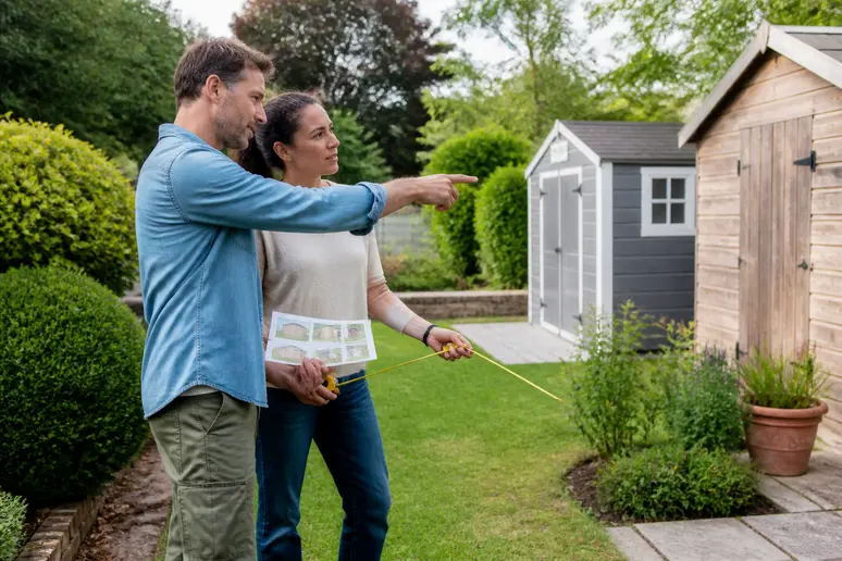 Un couple discute le choix d'un abri de jardin pour outils dans leur jardin.