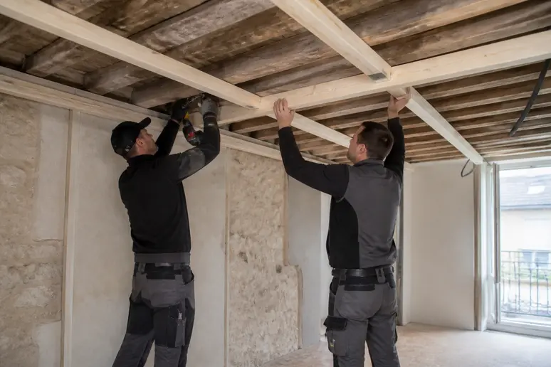 Installation d'une ossature bois pour un faux plafond suspendu par des ouvriers.