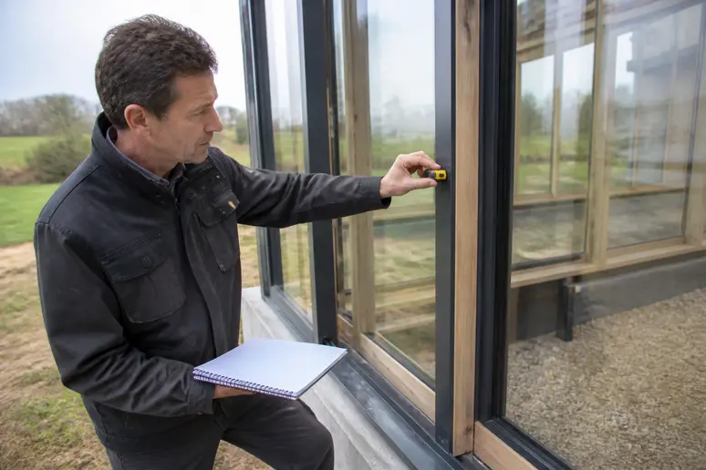 Expert vérifiant l'isolation d'une fenêtre pour une maison serre bioclimatique.