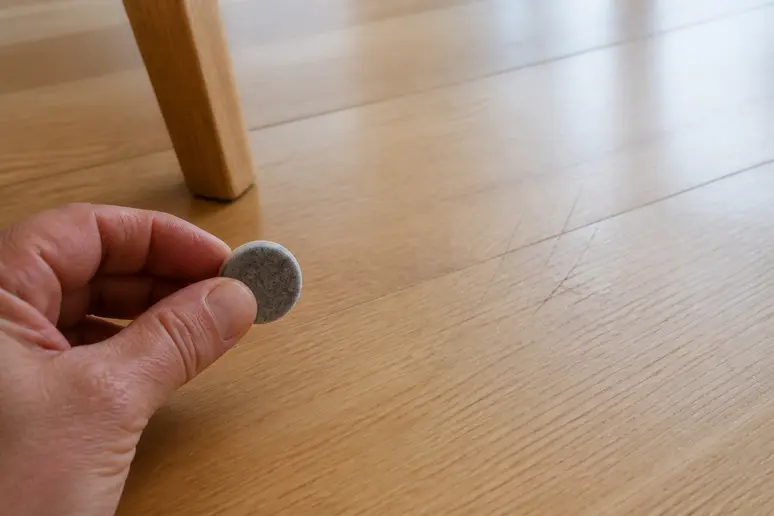 Prévention des défis du parquet clair : main avec patin en feutre près de rayures légères.