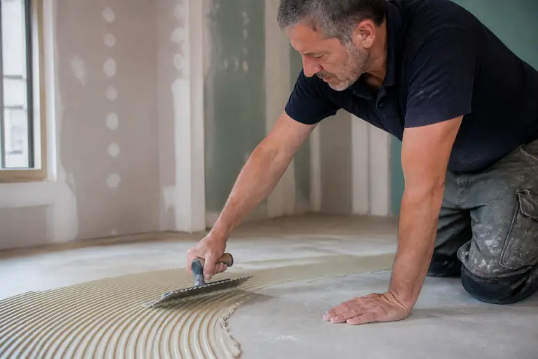 Installateur pose du parquet bois debout, application colle sur support propre.