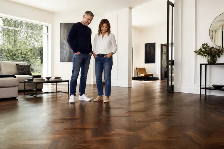 Un couple français admire un parquet bois foncé chaleureux, avec une belle luminosité naturelle dans leur salon moderne.