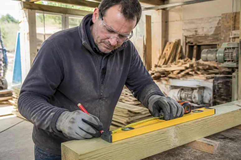 Un charpentier français mesure une poutre terrasse bois conforme aux normes.
