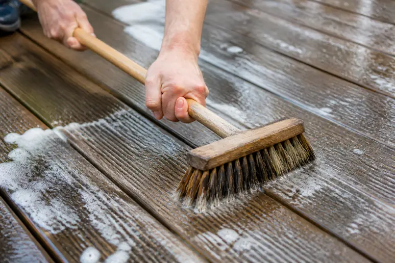 Nettoyage manuel d'une terrasse en bois avec un balai-brosse et de l'eau savonneuse