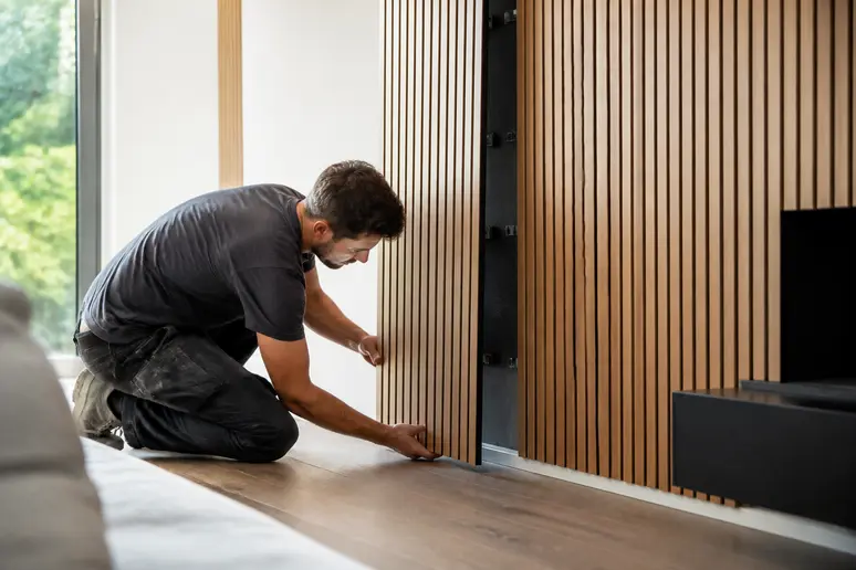 Pose de panneaux muraux bois décoratifs intérieurs par un artisan dans une pièce à vivre