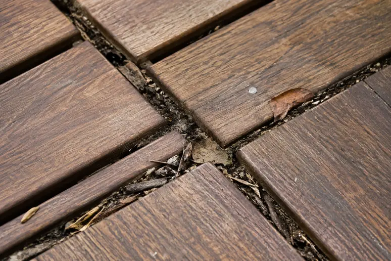 Saletés et débris accumulés dans les croisillons d'un caillebotis bois de terrasse