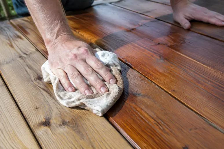 Un chiffon propre retire le surplus de saturateur sur une lame de terrasse bois