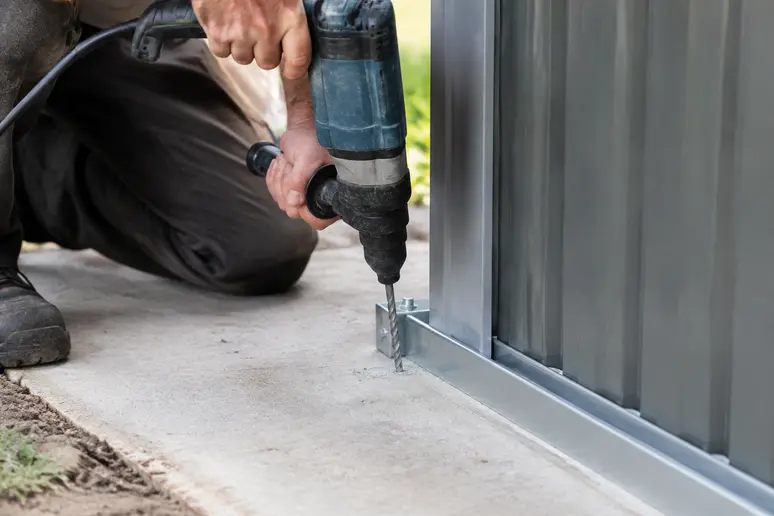 Utilisation d'un perforateur pour percer la dalle béton avant la pose du kit d'ancrage abri de jardin