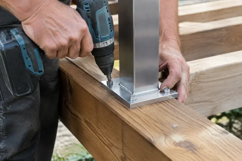 Fixation d'un poteau de rambarde de terrasse en bois sur une lambourde porteuse avec une vis inox.