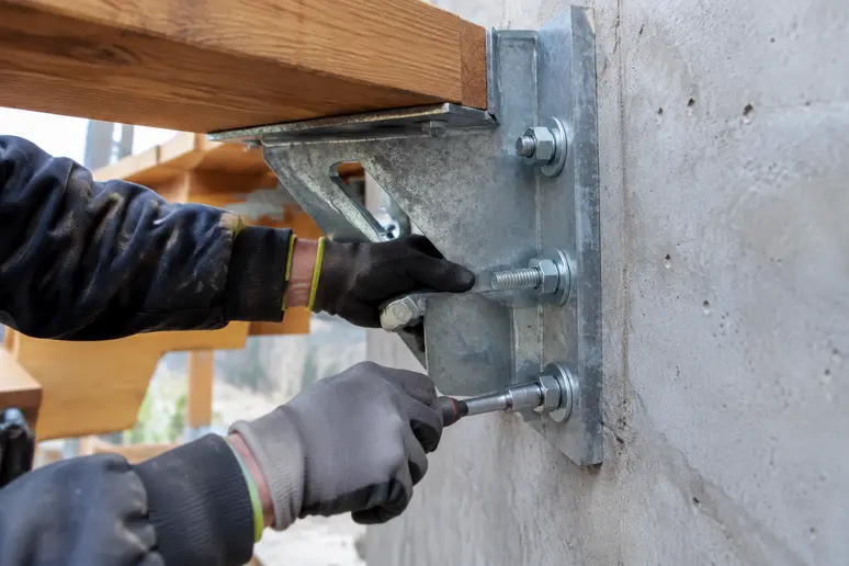 Pose de sabots à ailes et goujons d'ancrage sur le mur porteur pour une terrasse suspendue en bois.